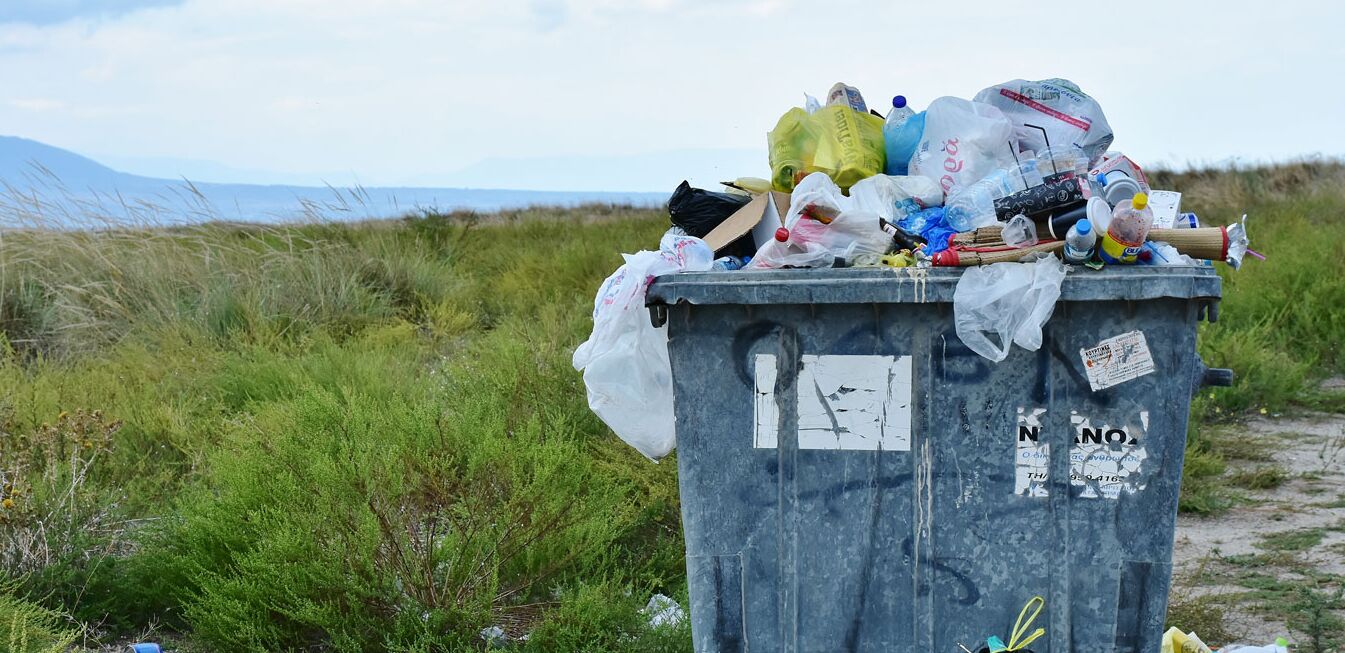 Überfüllte Tonne mit Plastikabfällen auf einem Feld