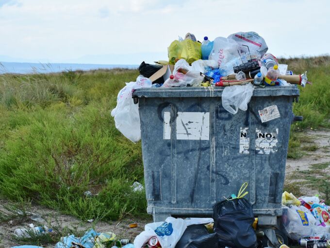 Überfüllte Tonne mit Plastikabfällen auf einem Feld